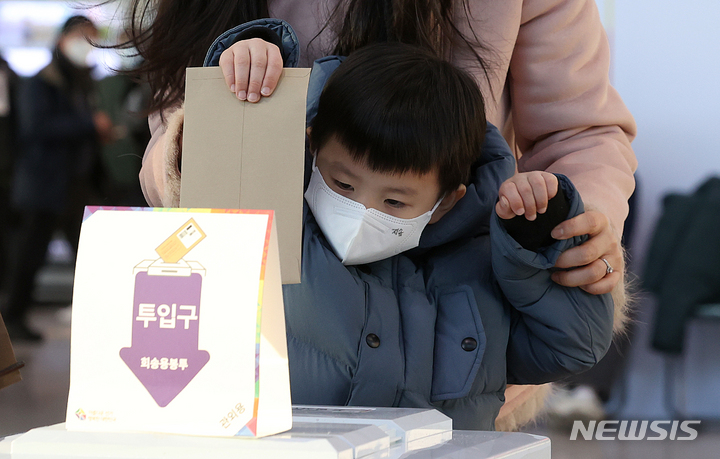 [서울=뉴시스] 김병문 기자 = 제20대 대통령선거 사전투표 이틀째인 지난 5일 오후 서울역 설치된 남영동 사전투표소에서 한 어린이가 어머니의 투표용지를 투표함에 넣고 있다. 2022.03.09. dadazon@newsis.com