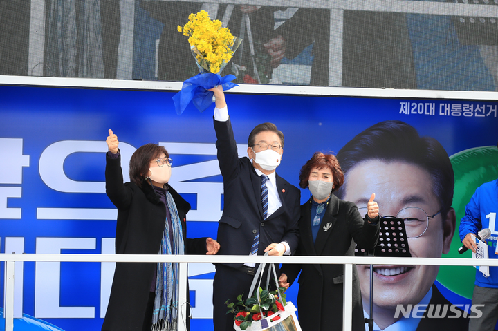 [제주=뉴시스] 우장호 기자 = 이재명 더불어민주당 대선후보가 7일 오전 제주시 동문시장 인근 광장에서 열린 '놀멍쉬멍 평화 제주! 느영나영 모두를 위해 이재명!' 유세에서 지지를 호소한 뒤 선물로 받은 유채꽃을 흔들어 보이고 있다. 이 후보는 이날 하루 동안 제주를 시작으로 부산, 대구, 대전, 충북 유권자들을 차례로 만나면서 막바지 유세 일정을 소화할 예정이다. 2022.03.07. woo1223@newsis.com