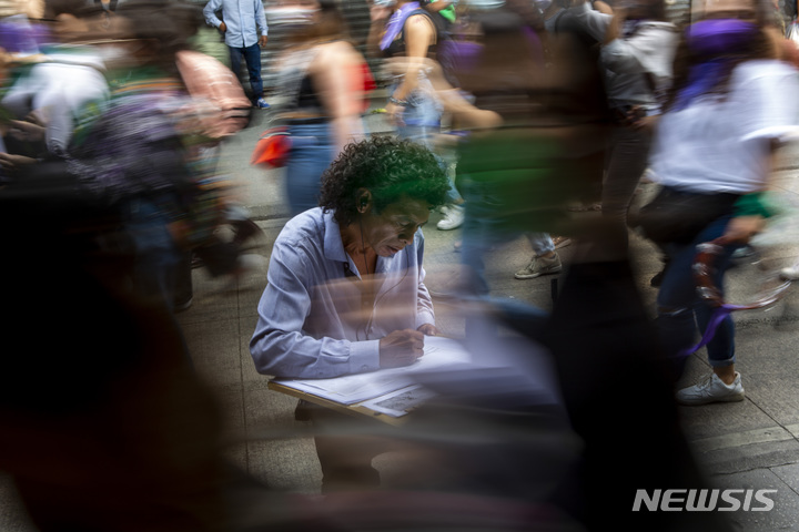 [과테말라시티=AP/뉴시스]과테말라시티에서 8일 한 거리 예술가가 세계 여성의 날을 맞아 행진하는 여성들의 모습을 스케치하고 있다. 과테말라 의회는 최근 멕시코, 아르헨티나, 콜롬비아 등 중남미에서 낙태에 대한 접근성을 점차 확대하는 추세에 역행, 낙태 시술을 한 여성에 대한 징역형을 최대 3년에서 10년으로 강화했다. 2022.3.10 