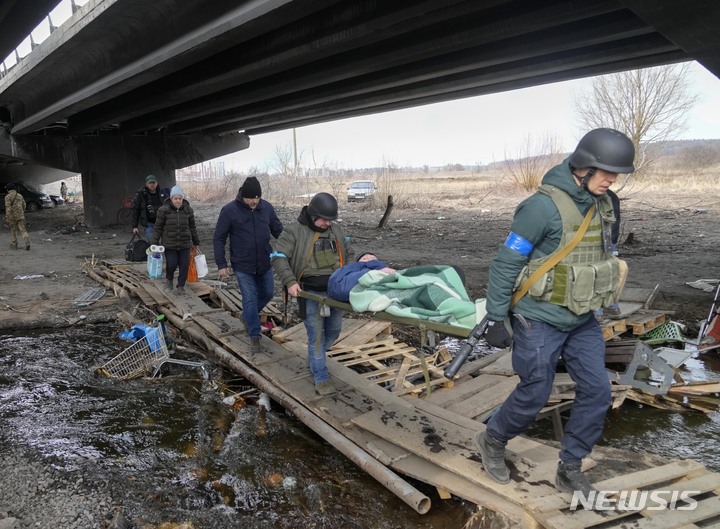[이르핀=AP/뉴시스] 12일(현지시간) 우크라이나 군인들이 이르핀 마을에서 노인을 들것에 실어 임시 통로를 건너고 있다. 이곳 다리는 러시아군의 공격으로 파괴돼 주민들은 임시 통로를 통해 이동하고 있다. 2022.03.13.