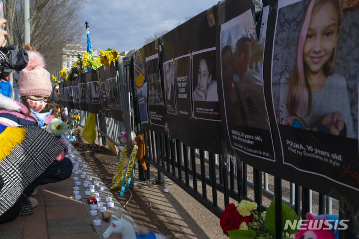 [워싱턴=AP/뉴시스] 13일 워싱턴 백악관 근처 라파예트 공원에서 열린 러시아의 우크라이나 침공 반대 시위 중 펜스에 전쟁 희생자들의 사진과 표지판들이 걸려있다. 2022.03.13. *재판매 및 DB 금지