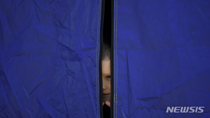 [시레트=AP/뉴시스] 14일(현지시간) 우크라이나와의 접경 도시인 루마니아 시레트에 도착한 한 우크라이나 소녀가 텐트 틈 사이로 밖을 내다보고 있다. 2022.03.15.