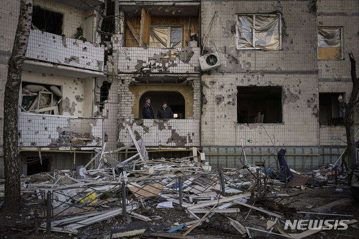 [키이우(우크라이나)=AP/뉴시스] 우크라이나 수도 키이우에서 지난 21일 폭격으로 파손된 아파트 주민들이 유리창을 고치려 하고 있다. 2022.3.29.