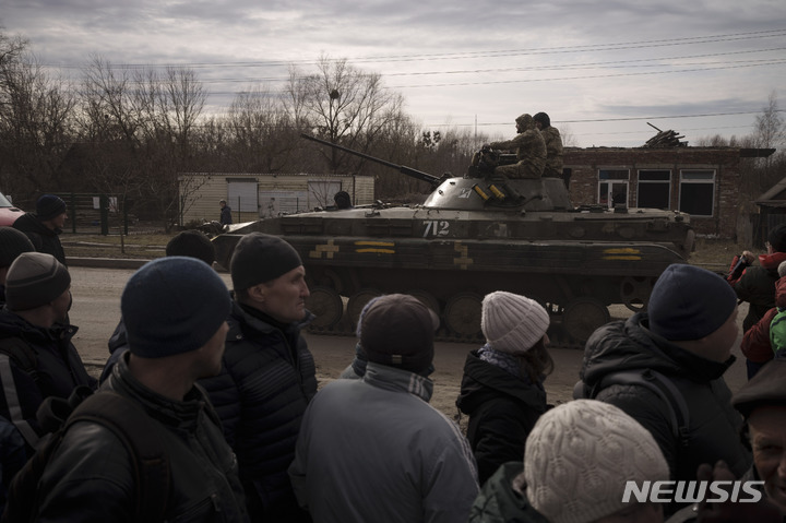 [트로스얀네츠=AP/뉴시스] 28일(현지시간) 우크라이나 트로스얀네츠 마을에서 구호 물품을 받기 위해 줄 선 주민들이 전차에 올라타고 지나가는 우크라이나 군인들을 바라보고 있다. 2022.03.29.
