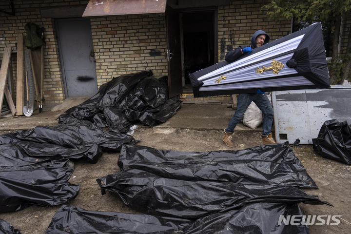 [부차=AP/뉴시스] 지난 6일(현지시간) 우크라이나 키이우 외곽 부차에서 경찰이 숨진 민간인들의 신원 확인 작업을 하는 동안 한 남성이 관을 옮기고 있다. 2022.04.14.