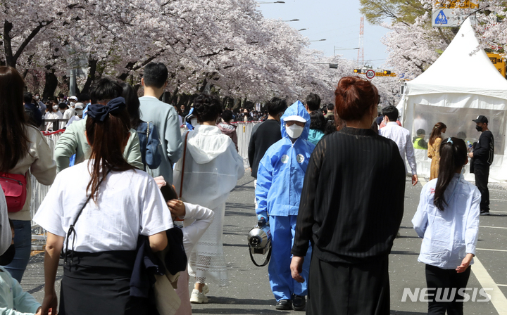 [서울=뉴시스] 최진석 기자 = 10일 서울 영등포구 여의도 윤중로 벚꽃길에서 영등포구 방역 관계자가 코로나19 확산 방지를 방역을 위해 상춘객들 사이를 지나고 있다. 2022.04.10. myjs@newsis.com