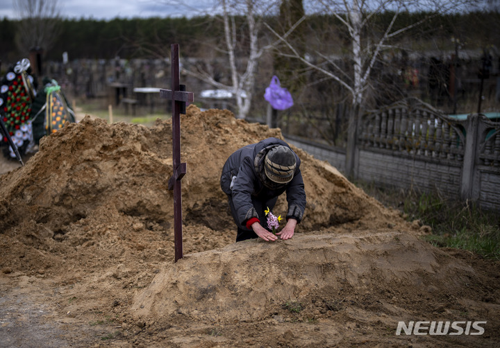 [부차=AP/뉴시스] 19일(현지시간) 우크라이나 부차에서 한 여인이 남편의 무덤에 꽂을 꽂고 있다. 남편은 러시아의 점령 기간 동안 치료를 받지 못해 숨진 것으로 알려졌다. 2022.04.20