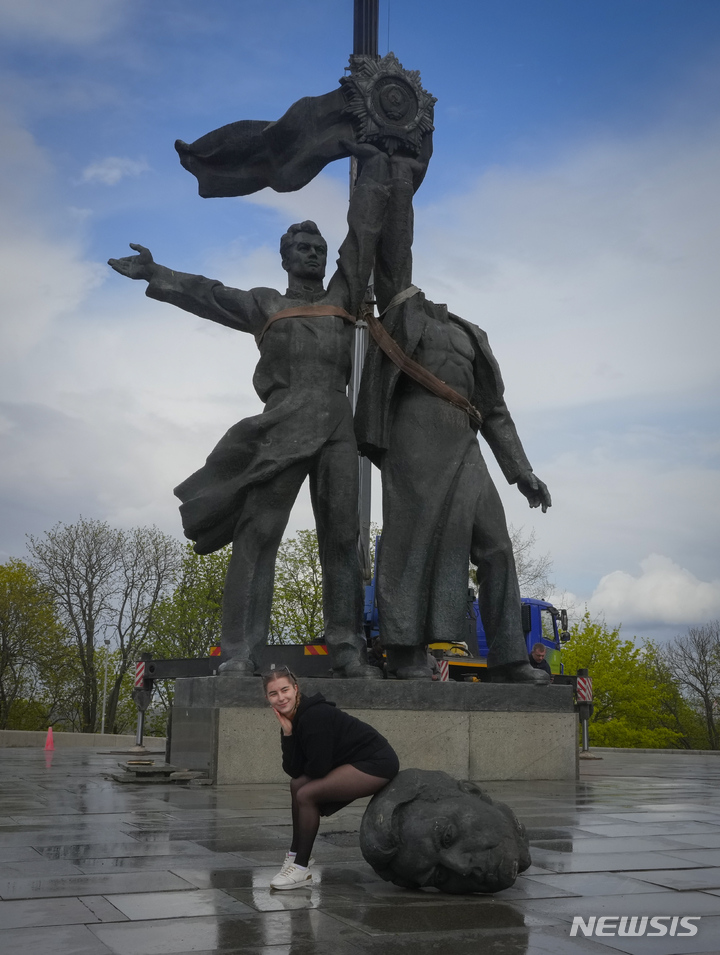 [키이우=AP/뉴시스] 지난달 26일(현지시간) 우크라이나 키이우에서 한 여성이 철거 중인 구소련 시대의 우호 상징 동상에 앉아 기념 촬영을 하고 있다. 2022.05.30.