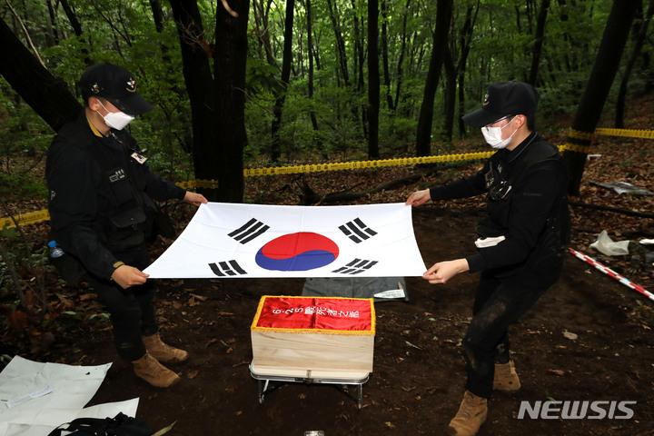 [포천=뉴시스] 백동현 기자 = 지난 16일 경기 포천시 소흘읍 일대 야산에서 국방부 유해발굴감식단 대원들이 발견된 유해를 오동나무 관에 넣고 태극기로 관포하고 있다. 2022.06.24. livertrent@newsis.com
