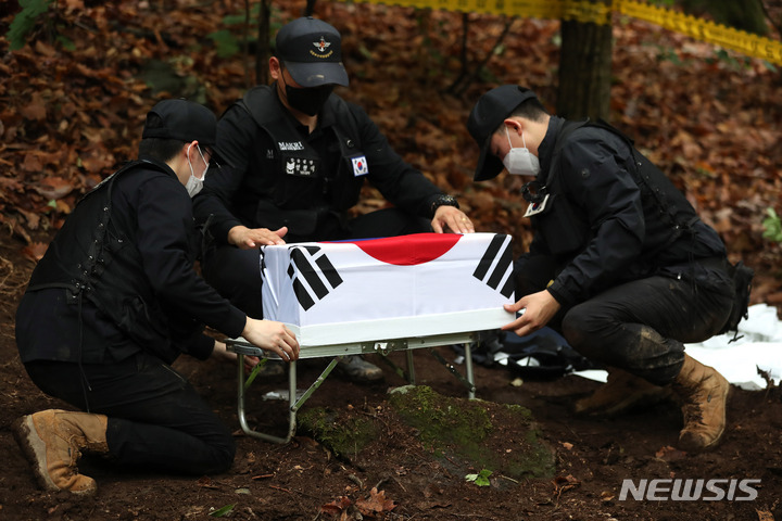 [포천=뉴시스] 백동현 기자 = 지난 16일 경기 포천시 소흘읍 일대 야산에서 국방부 유해발굴감식단 대원들이 발견된 유해를 오동나무 관에 넣고 태극기로 관포하고 있다. 2022.06.24. livertrent@newsis.com