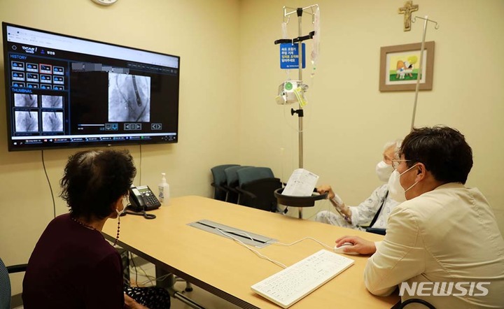 [서울=뉴시스]서울성모병원 심뇌혈관병원(병원장 장기육 교수) 타비팀이 판막주위 누출과 대동맥 인공판막 기능부전이 복합적으로 발생한 고령의 환자를 대상으로 국내에서 처음으로 타비(TAVI) 시술로 치료했다. 장 교수가 퇴원 전 환자와 보호자에게 시술 결과를 설명하고 있다. (사진= 서울성모병원 제공) 2022.07.07