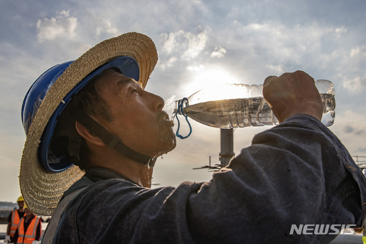 [충칭=신화/뉴시스]지난 11일 중국 남서부 충칭(重慶)의 장베이(江北)국제공항 터미널 건설공사 현장에서 노동자 한 명이 물을 마시고 있다. 맹렬한 폭염으로 중국이 주요 제조업들이 밀집한 지역의 기업과 가정에 전력을 덜 쓰도록 호소할 수밖에 없게 됐다고 CNN이 13일(현지시간) 보도했다. 2022.7.14