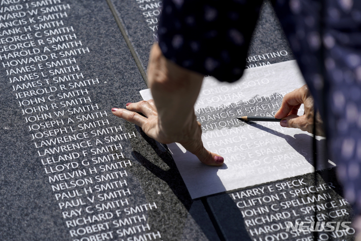 [워싱턴=AP/뉴시스] 27일(현지시간) 미국 워싱턴D.C. 한국전 참전용사 기념공원에 설치된 추모의 벽에서 한국전 전사자 유가족이 종이와 연필로 전사자의 이름 탁본을 뜨고 있다. 2022.07.28. 