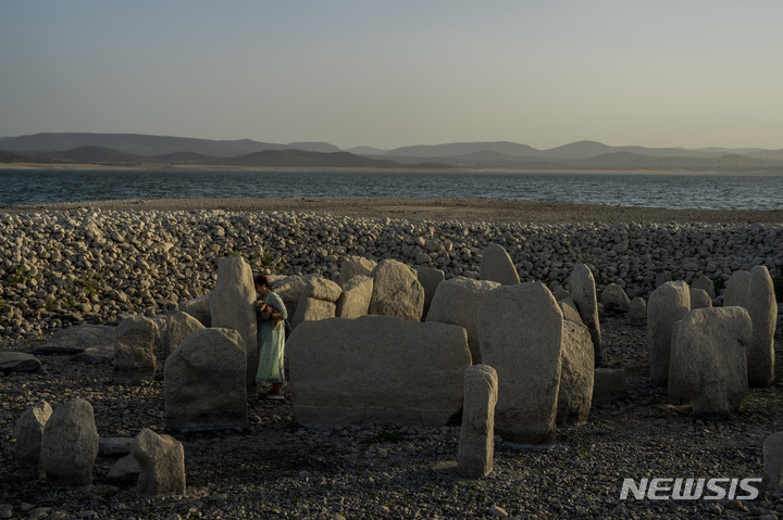 [마누페르난데즈=AP/뉴시스] 13일(현지시간) 스페인 서부지역 엘 고르도에 발데카냐스 저수지에 극심한 가뭄으로 인해 나타난 거석 기념물 '과달페랄 고인돌' 옆에 아말리 가르시아(54)가 서 있다. 세 번의 기록적인 폭염과 적은 강수량으로 인해 스페인 저수지가 일주일째 말라있다. 60년 만에 2번째로 찾아온 가뭄은 건조한 겨울에 찾아왔던 첫번째 가뭄보다 일찍 시작된 것으로 알려졌다. 2022.08.24.