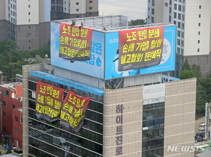 [서울=뉴시스] 김금보 기자 = 전국민주노동조합총연맹 공공운수노조 화물연대 조합원들이 지난 16일 오전 서울 강남구 하이트진로 본사 옥상에 대형 현수막을 설치하고 점거농성을 하고 있다. 2022.08.16. kgb@newsis.com