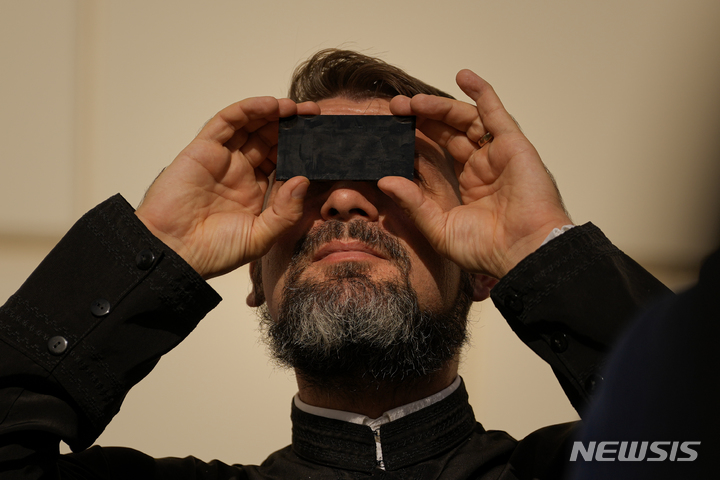 [루마니아=AP/뉴시스] 25일(현지시간) 루마니아 부쿠레슈티에서 한 신부가 부분일식을 보고 있다. 2022.10.26.