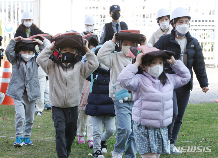 [서울=뉴시스] 김명원 기자 =지난해 11월16일 서울 종로구 정부서울청사에서 열린 재난대응안전한국훈련에서 어린이들이 책가방을 머리에 이고 대피훈련을 하고 있다. 2022.11.16. kmx1105@newsis.com
