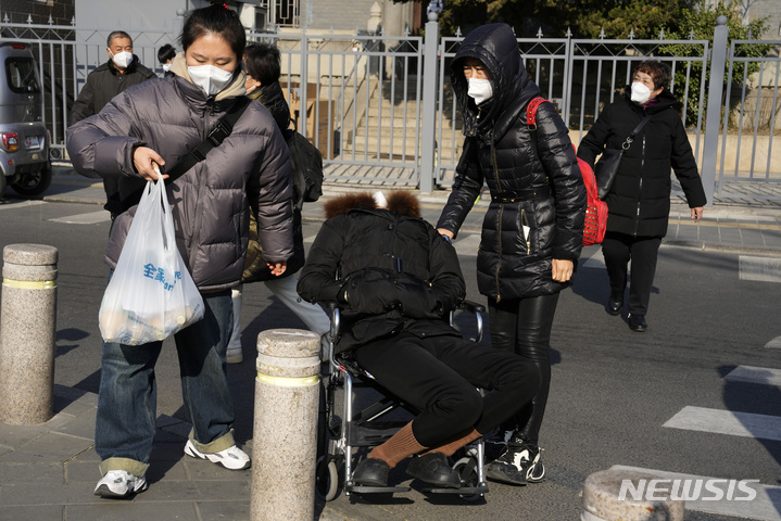 [베이징=AP/뉴시스] 9일 중국 베이징의 마스크를 쓰고 휠체어에 앉은 한 노인이 가족의 부축을 받으며 병원을 방문하고 있다. 중국은 일상 회복을 위한 '제로 코로나' 정책을 사실상 폐지했으나 전문가들은 갑작스러운 방역 완화로 전 인구의 80~90%가 결국 코로나19에 감염될 수도 있다고 경고하고 있다. 2022.12.09.