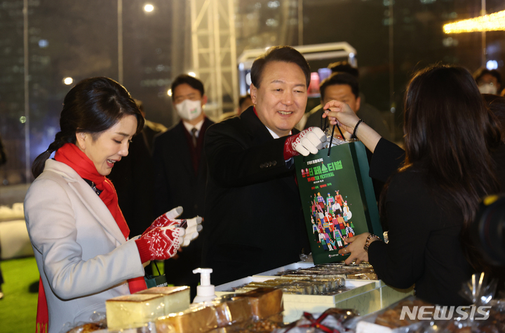 [서울=뉴시스] 홍효식 기자 = 윤석열 대통령과 부인 김건희 여사가 16일 서울 종로구 열린송현광장에서 열린 윈·윈터 페스티벌 개막식에서 에어돔 부스를 방문해 물건을 구입하고 있다. (대통령실통신사진기자단) 2022.12.16. yesphoto@newsis.com