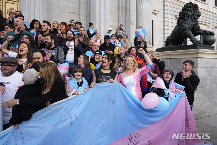 [마드리드=AP/뉴시스] 22일(현지시간) 스페인 마드리드 의회 밖에 모인 사람들이 성별을 자유롭게 바꾸게 해주는 트랜스젠더 법 발표에 환호하고 있다. 스페인 하원은 16세 이상의 시민이 의료 감독 없이 등록된 성별을 바꿀 수 있도록 하는 성전환 법을 통과시켰다. 이에 따라 12~13세 미성년자는 성별 변경을 위해 판사의 허가가 필요하고 14~16세 사이의 미성년자는 부모나 법률 대리인과 동행해야 한다. 2022.12.23.