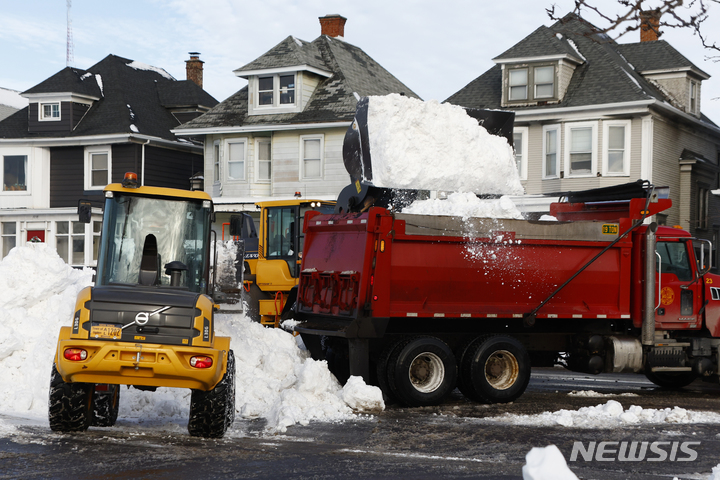 [버팔로=AP/뉴시스] 소형 크레인이 28일(현지시간) 뉴욕 버팔로에서 덤프 트럭에 눈을 쏟아 붓고있는 가운데, 직원들이 제설 작업을 하고 있다. 2022.12.30.