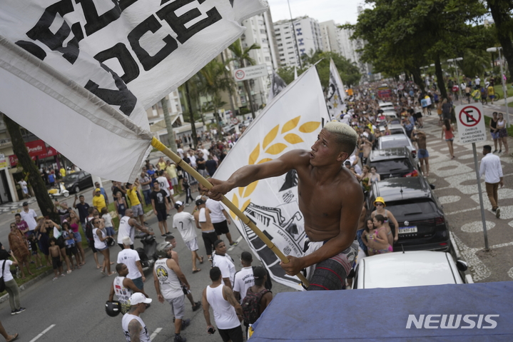 [산투스=AP/뉴시스] 3일(현지시간) 브라질 상파울루 외곽 산투스 거리에서 '축구 황제' 펠레의 장례 행렬이 이어지는 동안 한 남성이 산투스 FC의 깃발을 흔들며 펠레를 배웅하고 있다. 펠레는 아버지와 형제가 묻힌 '네크로폴 에큐메니카' 공동묘지에 안장됐다. 14층 높이의 이 묘지는 세계에서 가장 높은 공동묘지로 기네스북에 올라 있다. 2023.01.04.