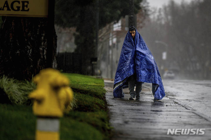 [캘리포니아=AP/뉴시스] 한 남성이 5일(현지시간) 캘리포니아 온타리오주에서 타프를 이용해 비를 막으며 거리를 갈아가고 있다. 2023.01.05.