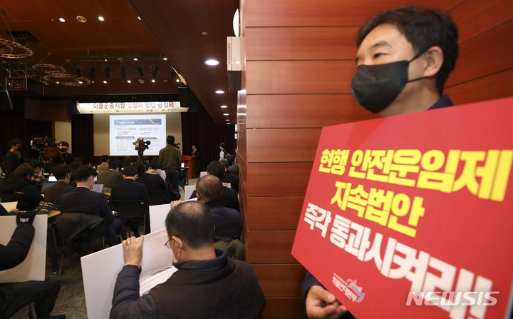 [서울=뉴시스] 최진석 기자 = 민주노총 공공운수노조 화물연대본부 관계자가 18일 서울 중구 포스트타워에서 국토교통부 주최로 진행된 '화물운송시장 정상화 방안 공청회'에서 안전운임제 지속 촉구 피켓을 들고 이태형 한국교통연구원 선임연구위원의 발제를 듣고 있다. 2023.01.18. myjs@newsis.com