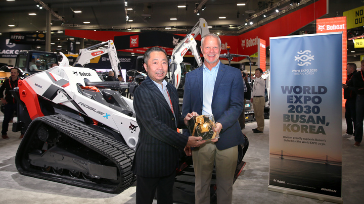 [서울=뉴시스] 박정원 두산그룹 회장이 지난 15일 미국 라스베이거스에서 열린 '콘엑스포 2023'을 찾아 무인 전기 콘셉트 로더 '로그 X' 와 부산엑스포 유치를 기원하는 배너 앞에서 마이크 볼웨버 북미 지역장에게 두산일두 기념패를 전달하고 있다.(사진=두산 제공) 2023.03.19 photo@newsis.com *재판매 및 DB 금지