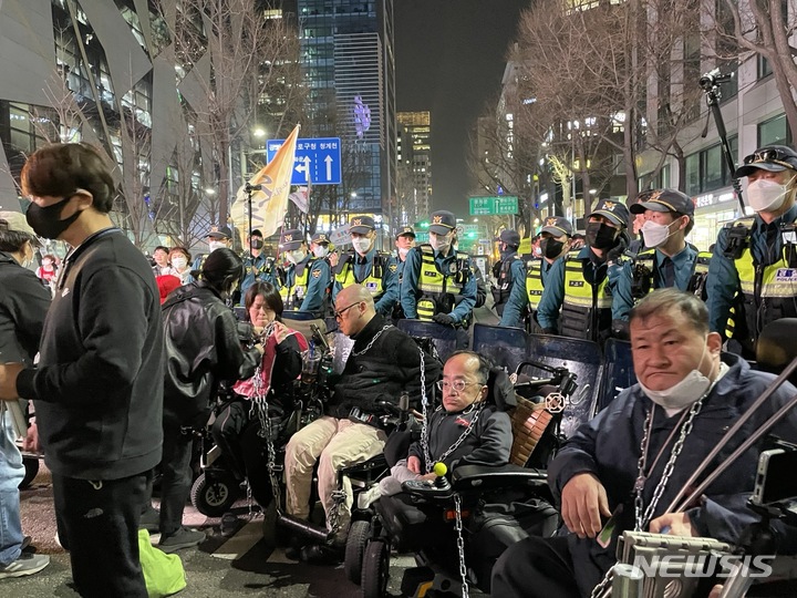 [서울=뉴시스] 임철휘 기자 = 전국장애인차별철폐연대 활동가들이 23일 오후 7시30분께 몸에 쇠사슬을 묶고 휠체어로 벽을 만들어 서울 중구 무교로 차로를 막아서고 있다. 2023.03.23. fe@newsis.com