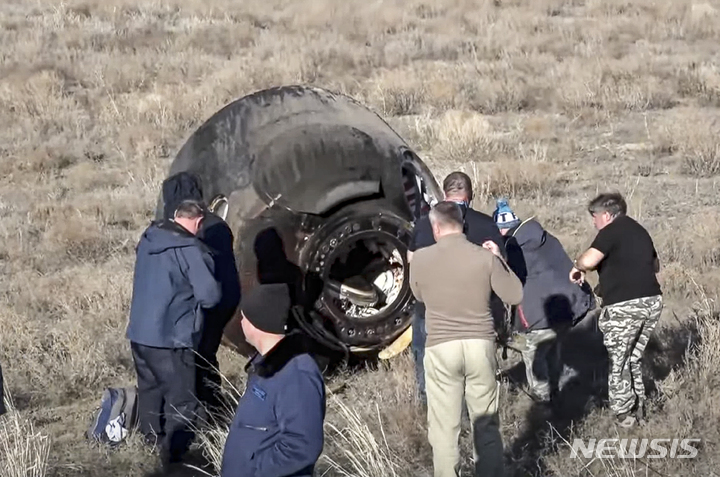 [AP/뉴시스] 러시아 우주당국 로스코스모스 배포 사진으로 28일 우주비행사를 한 명도 태우지 않고 빈 채로 카자흐스탄 초원에 낙하 귀환한 소유즈 캡슐을 전문가들이 수거하고 있다
