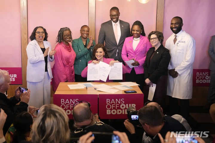 [버밍햄(미시간주)=AP/뉴시스] 그레첸 휘트머 미국 미시간주 주지사(가운데)가 5일(현지시간) 미시간주 버밍햄에서 낙태 금지 폐지법에 서명한 뒤 법안을 들어보이고 있다. 미시간주에서 낙태 금지법은 지난 1931년 제정됐다. 2023.04.06