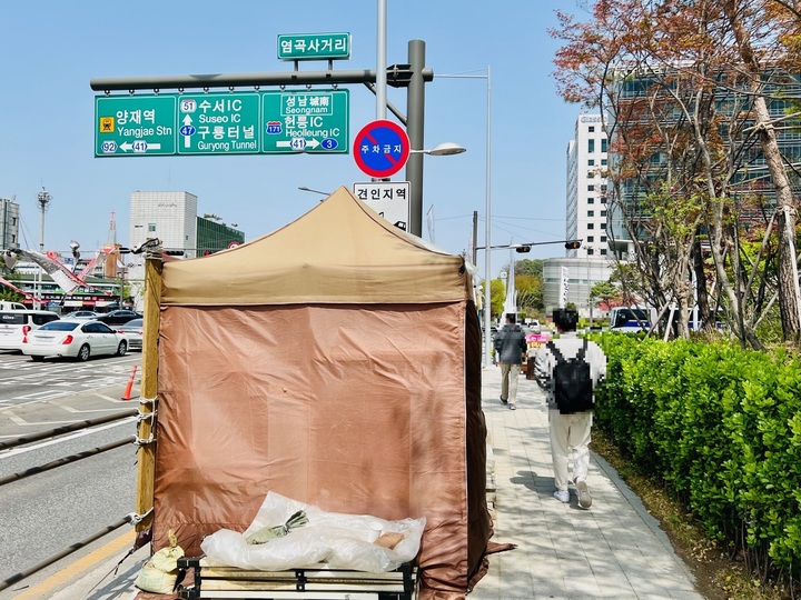 [서울=뉴시스] 서울 서초구 양재동에 있는 현대자동차그룹 본사 사옥 앞 도로에 설치된 불법 천막. 보행자 통로 대부분을 막고 있고 보행자 불편을 야기하는 한편, 내부 취식 등으로 시민 안전까지 위협한다는 지적이 나온다. (사진=독자 제공) 2023.04.13 photo@newsis.com *재판매 및 DB 금지