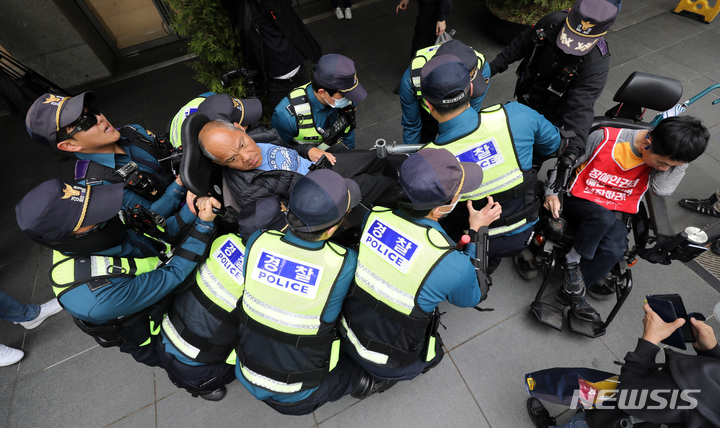[서울=뉴시스] 김금보 기자 = 장애인의날인 20일 경찰이 서울 영등포구 63컨벤션센터 앞에서 열린 '장애인의날을 거부하는 자들의 장애인차별철폐의날 기념식'에서 전동휠체어 고장으로 이동이 어려워진 집회 참가자를 들어 이동시키고 있다. 2023.04.20. kgb@newsis.com