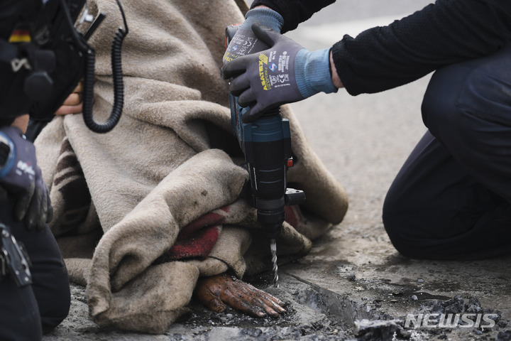 [베를린=AP/뉴시스] 24일(현지시간) 독일 베를린에서 기후 운동가가 정부의 기후 정책에 반대하기 위해 강력 접착제로 자신의 몸을 도로에 붙여 시위를 벌인 가운데 경찰이 장비를 이용해 뜯어내려 하고 있다. 2023.04.25.