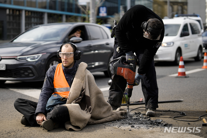 [베를린=AP/뉴시스] 24일(현지시간) 독일 베를린에서 기후 운동가가 정부의 기후 정책에 반대하기 위해 강력 접착제로 자신의 몸을 도로에 붙여 시위를 벌인 가운데 경찰이 장비를 이용해 뜯어내려 하고 있다. 2023.04.25.