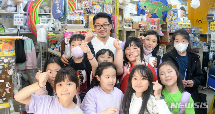 [전주=뉴시스] 김얼 기자 = 제101회 어린이날을 하루 앞둔 4일 전북 전주시 전주북일초등학교 앞 사랑문구에서 임희택 사장이 문구점을 찾은 어린이들과 손가락 하트를 그리며 사진을 찍고 있다. 2023.05.04. pmkeul@nwsis.com