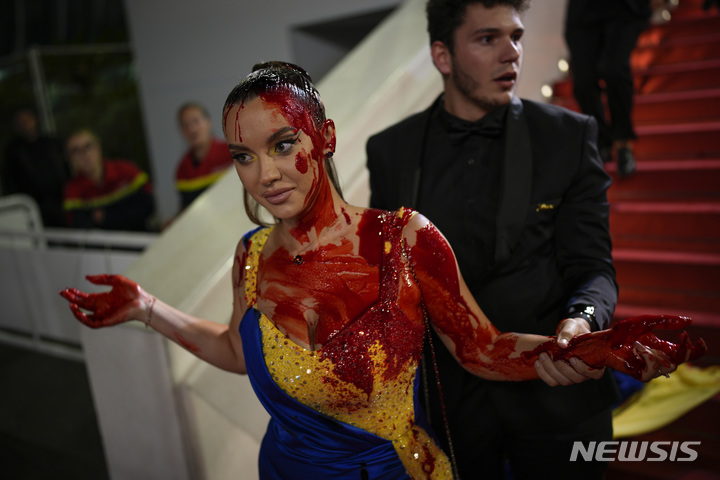 [서울=AP/뉴시스] 우크라이나 국기 색 드레스를 입은 채 몸에 빨간색 액체를 뿌리는 시위를 벌인 여성이 보안요원 제지로 퇴장당하고 있다.