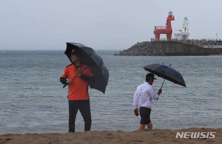 [제주=뉴시스] 우장호 기자 = 제주도와 남해안에 장맛비가 내리고 있는 가운데 월요일인 오는 26일부터 장마가 전국적으로 확대되겠다. 사진은 올해 첫 장맛비가 내리는 25일 오전 제주시 이호해수욕장에 우산을 쓴 수상안전요원과 시민이 걸어가고 있는 모습. 2023.06.23. woo1223@newsis.com