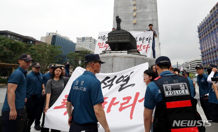 [서울=뉴시스] 조성봉 기자= 12일 오전 서울 종로구 광화문 이순신 동상 위에서 민주노총 조합원들이 ‘일본 후쿠시마 오염수 해양투기 반대’, ‘윤석열 대통령 퇴진’ 등 구호를 외치며 기습시위를 하고 있다. 경찰이 연행하려 하자 민주노총 조합원들이 스크럼을 짜고 구호를 외치고 있다. 2023.07.12. suncho21@newsis.com