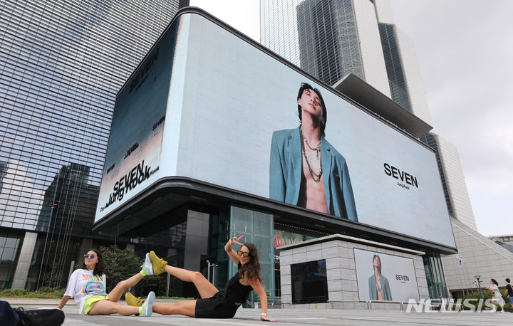 [서울=뉴시스] 황준선 기자 = 2023년 25일 오후 서울 강남구 코엑스 케이팝 스퀘어 전광판 앞에서 외국인 관광객들이 방탄소년단(BTS) 멤버 정국의 솔로 싱글 '세븐(SEVEN)'의 광고물을 배경으로 기념촬영을 하고 있다. 2023.07.25. hwang@newsis.com