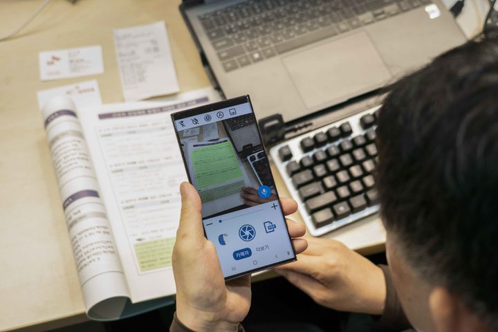 [서울=뉴시스] SK텔레콤은 7일부터 10일까지 부산 벡스코에서 열리는 ‘제1회 부산세계장애인대회’에 장애인을 위한 AI(인공지능) 서비스 3종을 소개하는 전시관을 운영한다고 6일 밝혔다. 사진은 시각장애인이 설리번A 앱을 활용해 책자와 영수증, 명함 등에 있는 글의 내용을 확인하는 모습.(사진=SKT). 2023.08.06 *재판매 및 DB 금지