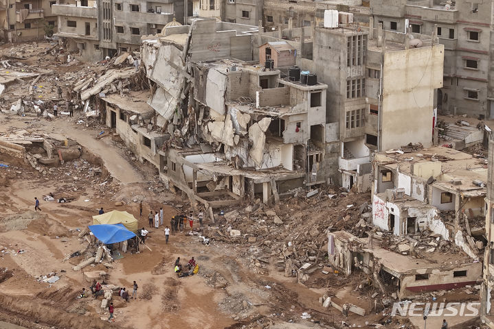 [데르나=AP/뉴시스] 대홍수 참사가 발생한 리비아 북동부 도시 데르나에서 구조대와 친지들이 지난 18일(현지시간) 무너진 건물 앞에 앉아 있다. 2023.09.21.