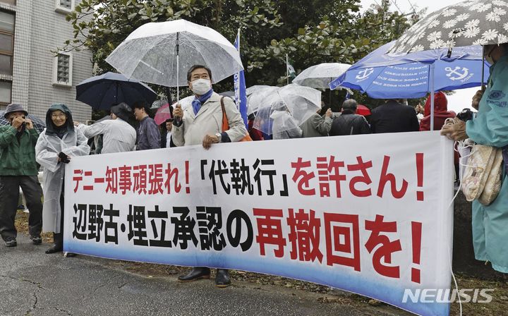 [오키나와=AP/뉴시스]일본 정부는 오키나와(沖縄)현의 미군 후텐마(普天間) 기지 이전 예정지인 나고(名護)시 헤노코(辺野古) 앞바다의 지반개량 공사를 10일 착수했다고 발표했다. 사진은 지난해 12월 20일 일본 오키나와 나하 법원 근처에서 시위대가 "(오키나와현) 다마키 지사 힘내라! 대집행 용서못해! 헤노코·매립 승인 재철회를!"이라고 쓰여진 현수막을 들고 있는 모습. 2024.01.10.