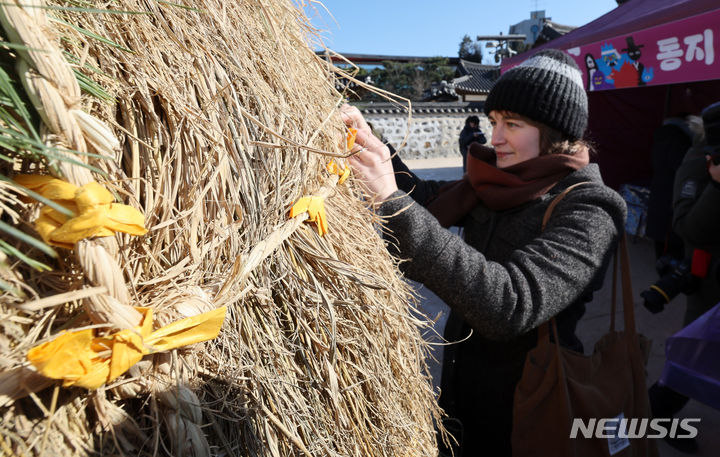 [서울=뉴시스] 조성우 기자 = 절기상 동지인 22일 오후 서울 중구 남산골 한옥마을에서 열린 '세시울림 (귀)신나는 동지' 행사를 찾은 한 외국인 관광객이 소원을 적은 종이를 달집에 달고 있다. 2023.12.22. xconfind@newsis.com