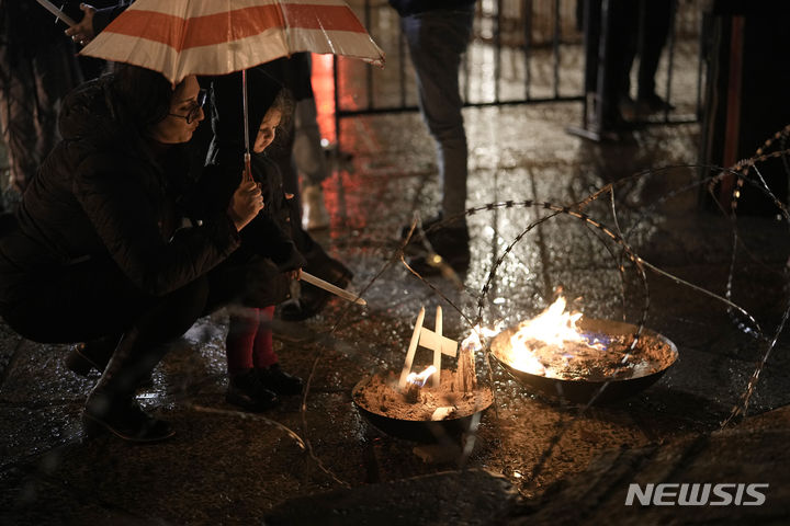 [베들레헴=AP/뉴시스] 23일(현지시각) 요르단강 서안지구 베들레헴에 있는 예수탄생 교회 인근 구유 광장에서 한 여성이 어린이와 함께 가자지구 희생자들을 기리기 위한 그리스도 성탄화 앞에 촛불을 밝히고 있다. 이스라엘-하마스 전쟁으로 예수 탄생지 베들레헴은 조용히 크리스마스를 맞이하고 있다. 2023.12.24.