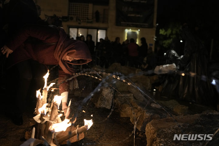 [베들레헴=AP/뉴시스] 23일(현지시각) 요르단강 서안지구 베들레헴에 있는 예수탄생 교회 인근 구유 광장에서 한 여성이 가자지구 희생자들을 기리기 위한 그리스도 성탄화 앞에 촛불을 밝히고 있다. 이스라엘-하마스 전쟁으로 예수 탄생지 베들레헴은 조용히 크리스마스를 맞이하고 있다. 2023.12.24.