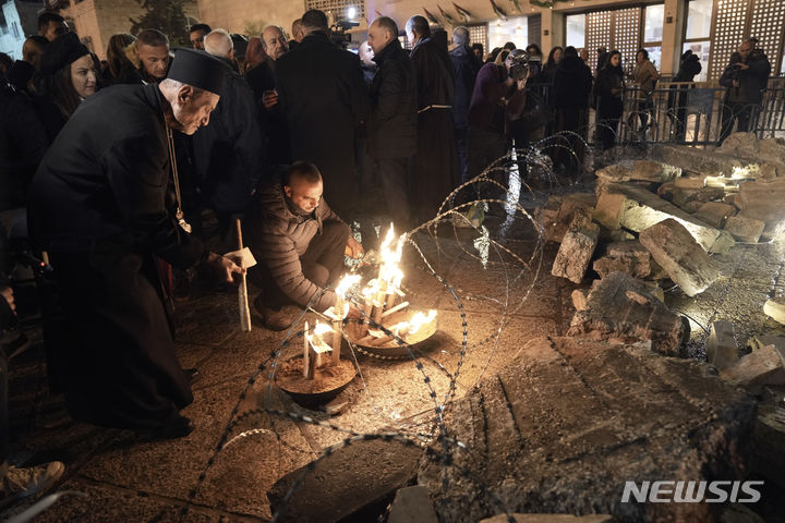 [베들레헴=AP/뉴시스] 23일(현지시각) 요르단강 서안지구 베들레헴에 있는 예수탄생 교회 인근 구유 광장에서 한 사제와 남성이 가자지구 희생자들을 기리기 위한 그리스도 성탄화 앞에 촛불을 밝히고 있다. 이스라엘-하마스 전쟁으로 예수 탄생지 베들레헴은 조용히 크리스마스를 맞이하고 있다. 2023.12.24.