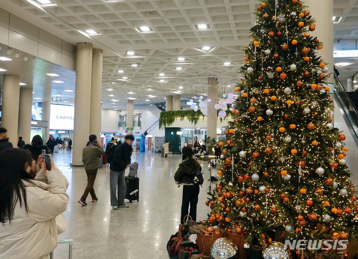 [제주=뉴시스] 오영재 기자 = 크리스마스 이브를 맞은 24일 오전 관광객들이 제주국제공항 도착장에 설치된 감귤트리를 찍고 있다. 2023.12.24. oyj4343@newsis.com 
