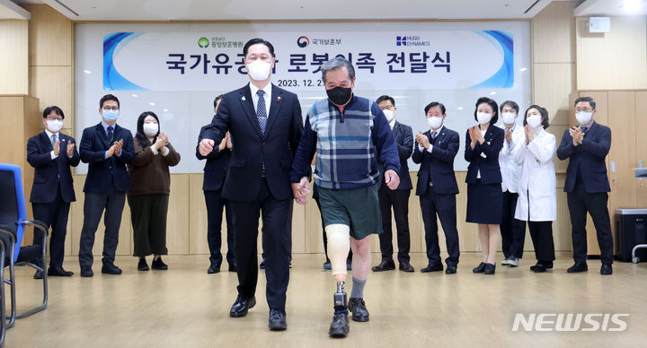 [서울=뉴시스] 김선웅 기자 = 이희완 국가보훈부 차관이 27일 서울 강동구 중앙보훈병원을 방문해 지뢰 사고로 다리를 잃은 장원종 국가유공자에게 로봇 의족을 전달한 후 함께 걷고 있다. 2023.12.27. mangusta@newsis.com